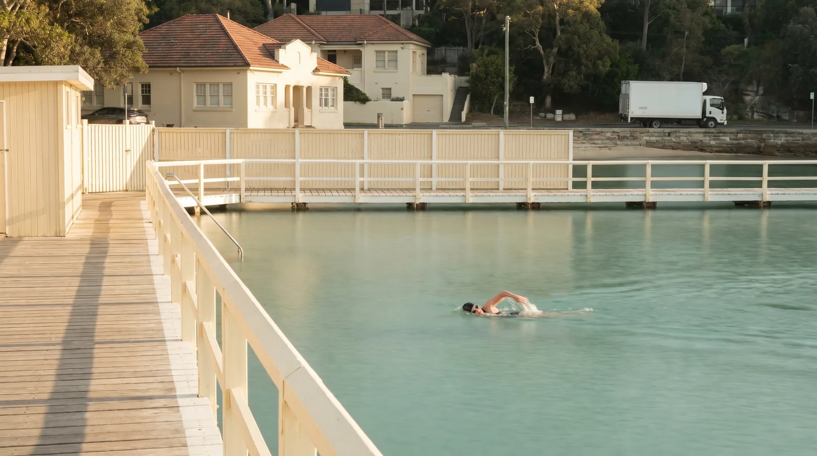 A lap swimmer in the flat green water of the harbour baths at 7am, timber boardwalk in the foreground
